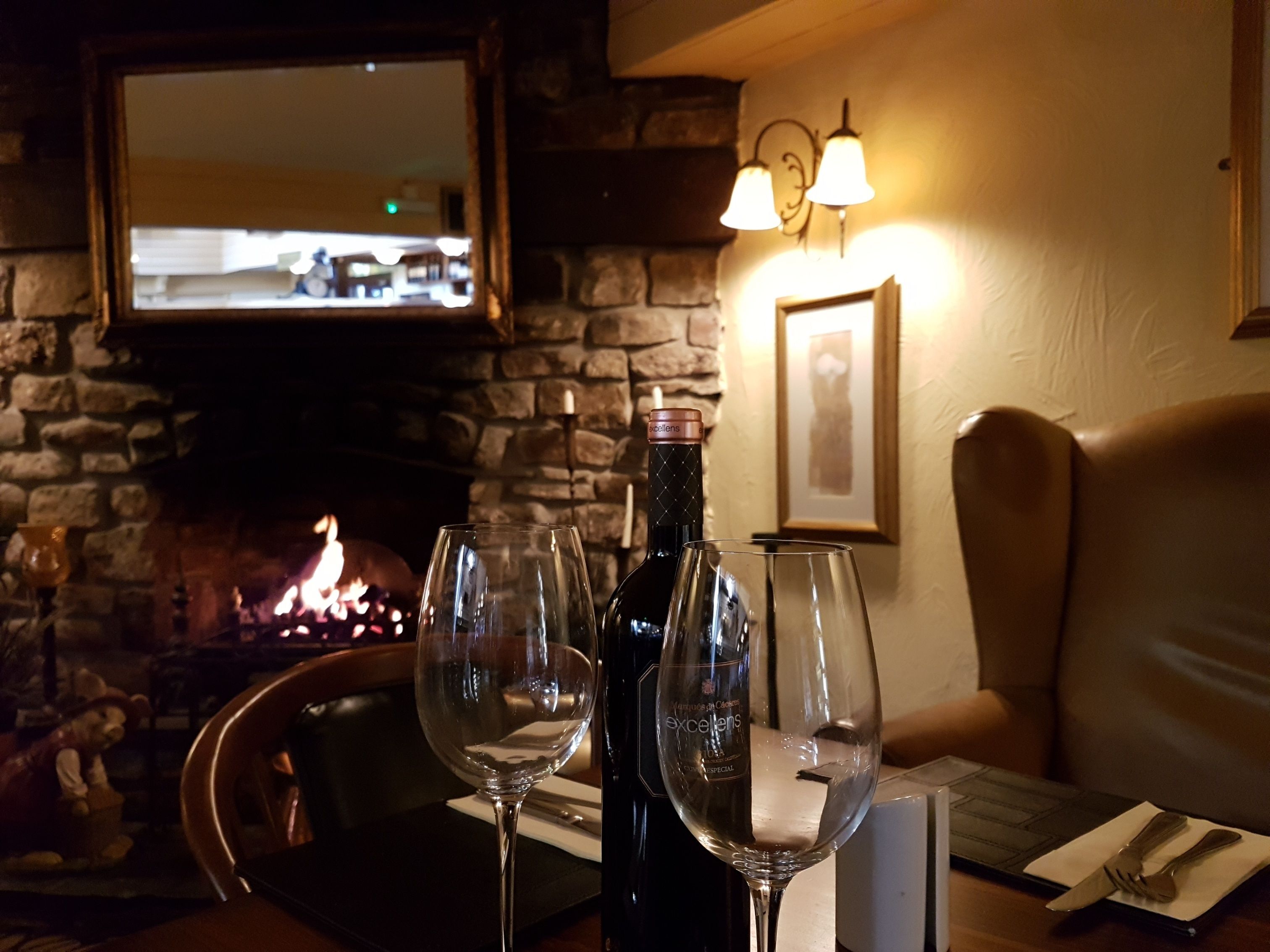 A cozy restaurant setting with a stone fireplace, wine glasses, and a bottle of wine on the table.