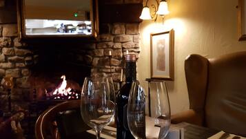 A cozy restaurant setting with a stone fireplace, wine glasses, and a bottle of wine on the table.