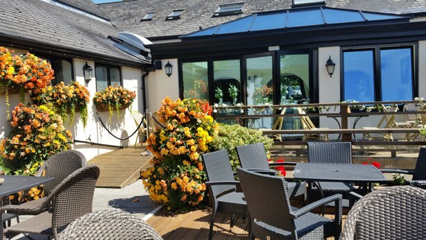 An outdoor seating area with wicker furniture and flower arrangements. - The Old Barn Inn (Newport)