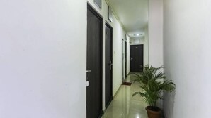 A narrow hallway with dark doors, a potted plant, and a tiled floor. - Golden Deluxe (New Delhi)