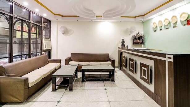 A hotel lobby with a brown sofa, a coffee table, a reception desk, and a wall with decorative plates. - Golden Deluxe (New Delhi)