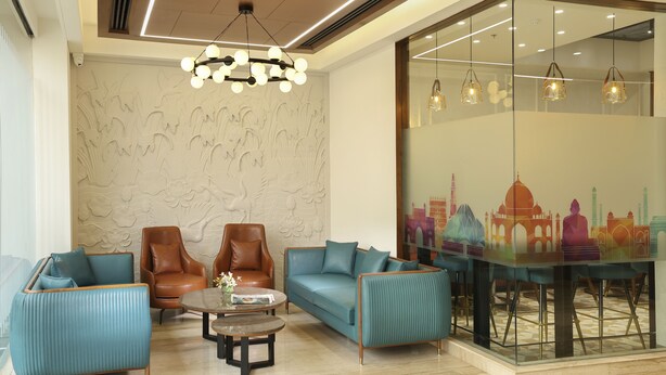 A modern lobby with seating arrangements, a decorative wall, and a glass partition with a cityscape mural. - Indus Biznotel (New Delhi)