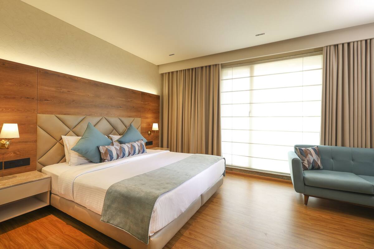 A modern hotel room with a large bed, a sofa, a nightstand, and a window with curtains.