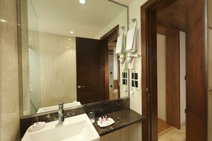 A modern bathroom with a large mirror, a white sink, and a dark marble countertop. - Indus Biznotel (New Delhi)