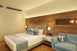 A modern hotel room with a large bed, two bedside tables, a sofa, and a wooden accent wall. - Indus Biznotel (New Delhi)