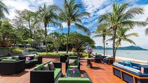 An outdoor seating area with wicker furniture and a wooden deck overlooking a beach. - Pattaya Sea Sand Sun Resort & Spa (Pattaya)