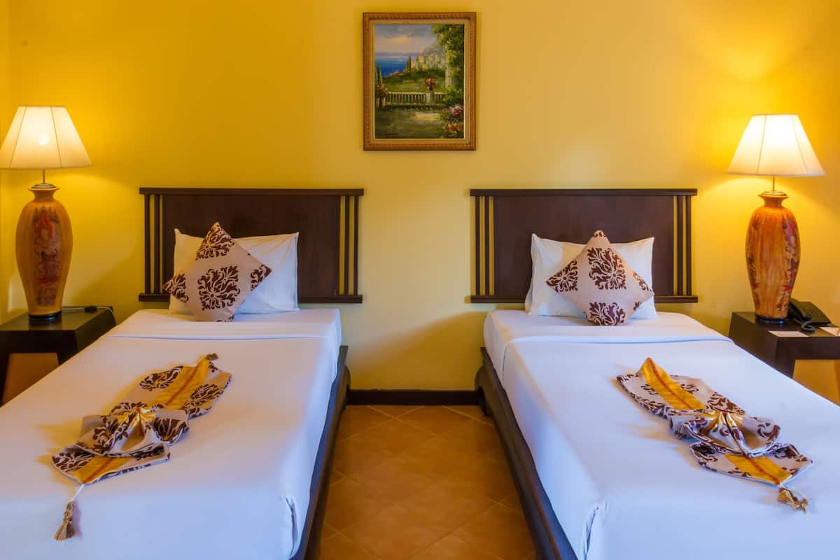 Una habitación de hotel con dos camas, cada una con una almohada estampada y una bufanda decorativa. Hay un cuadro en la pared sobre las camas.