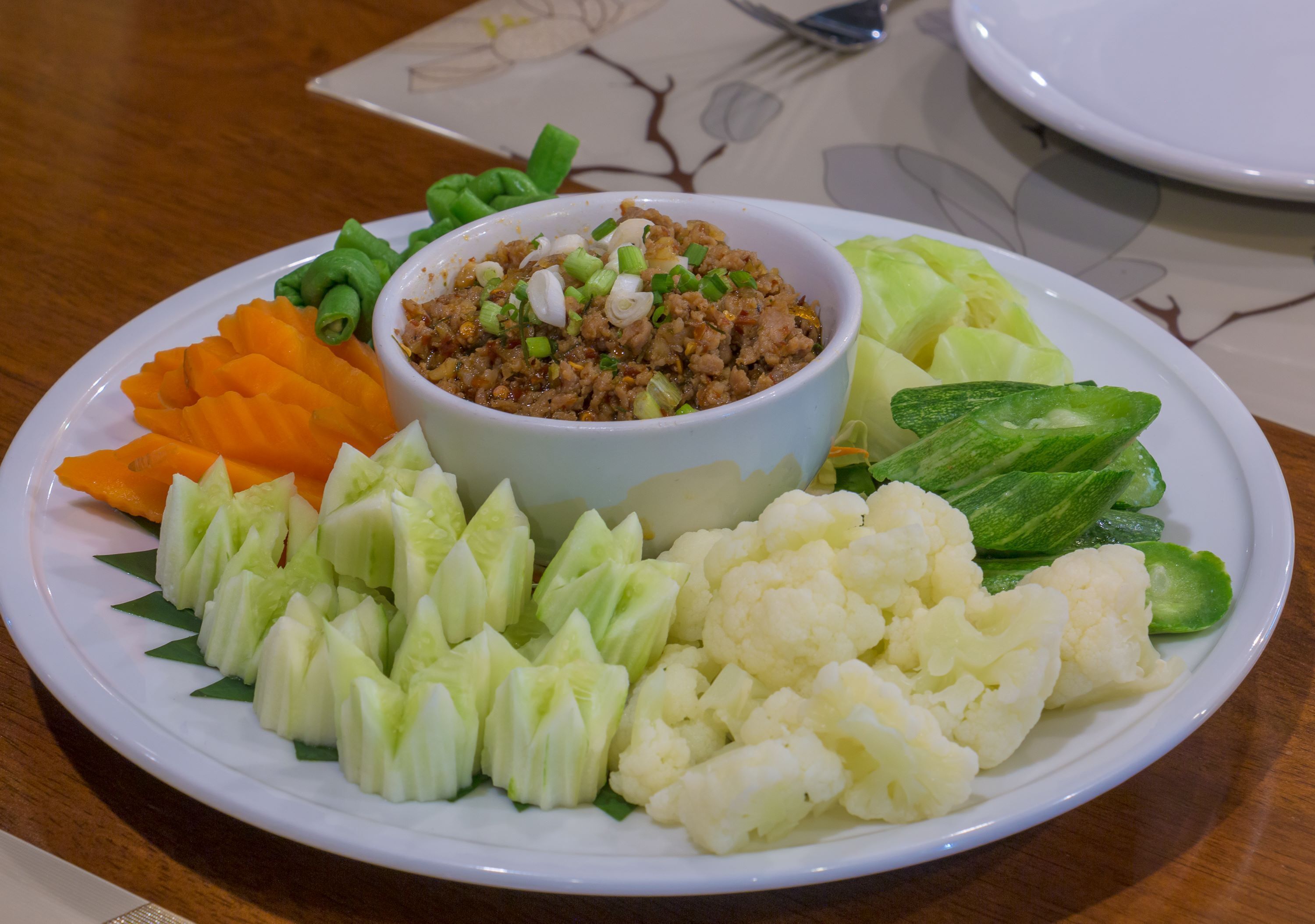 A plate with a bowl of minced meat, surrounded by sliced vegetables including carrots, cabbage, and cauliflower.