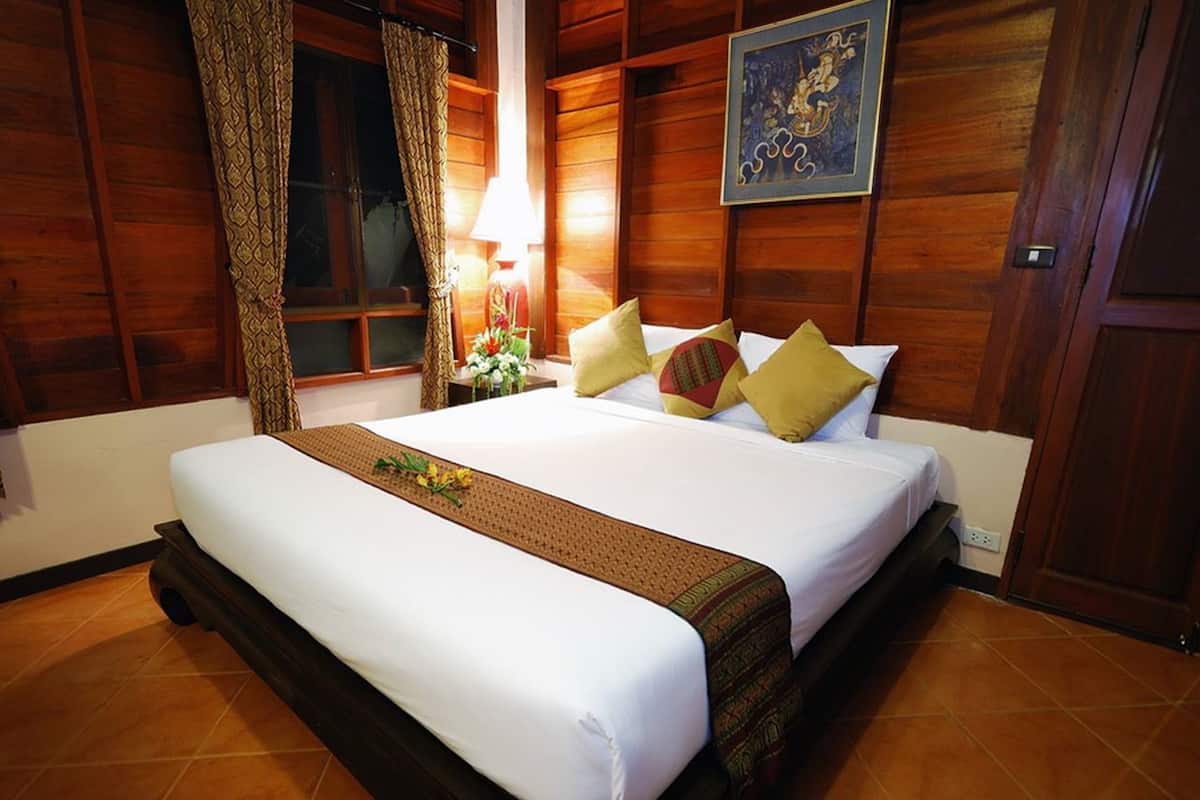 Una habitación de hotel con una cama grande, paredes de madera, una ventana con cortinas, una mesita de noche con lámpara y un cuadro enmarcado en la pared.