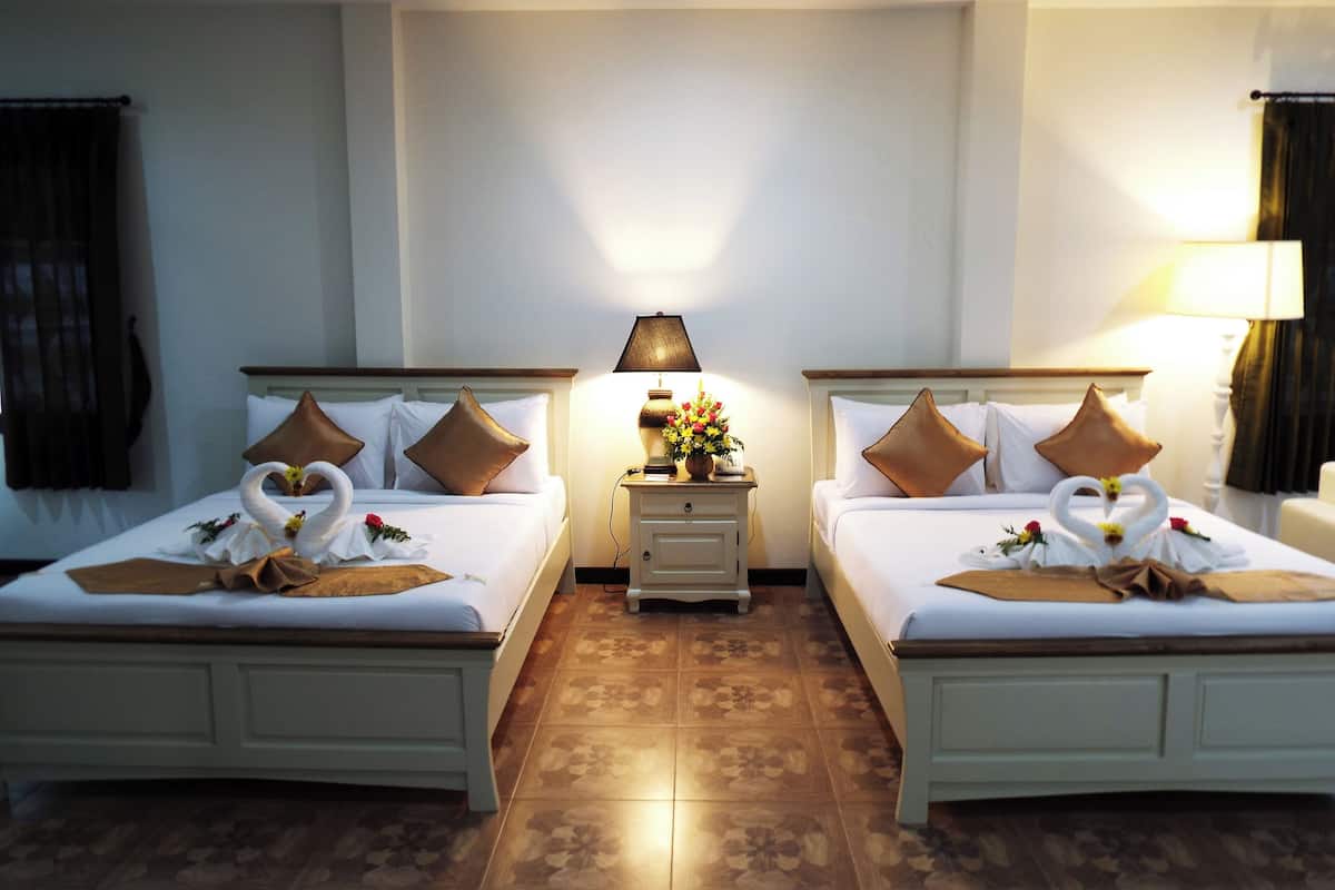 Habitación de hotel con dos camas, cada una decorada con almohadas con forma de cisne y un arreglo floral con forma de corazón.