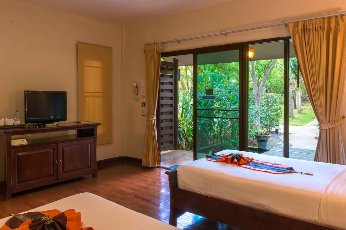 Habitación de hotel con cama, televisión sobre un mueble de madera y puerta corrediza de vidrio que da a un jardín.