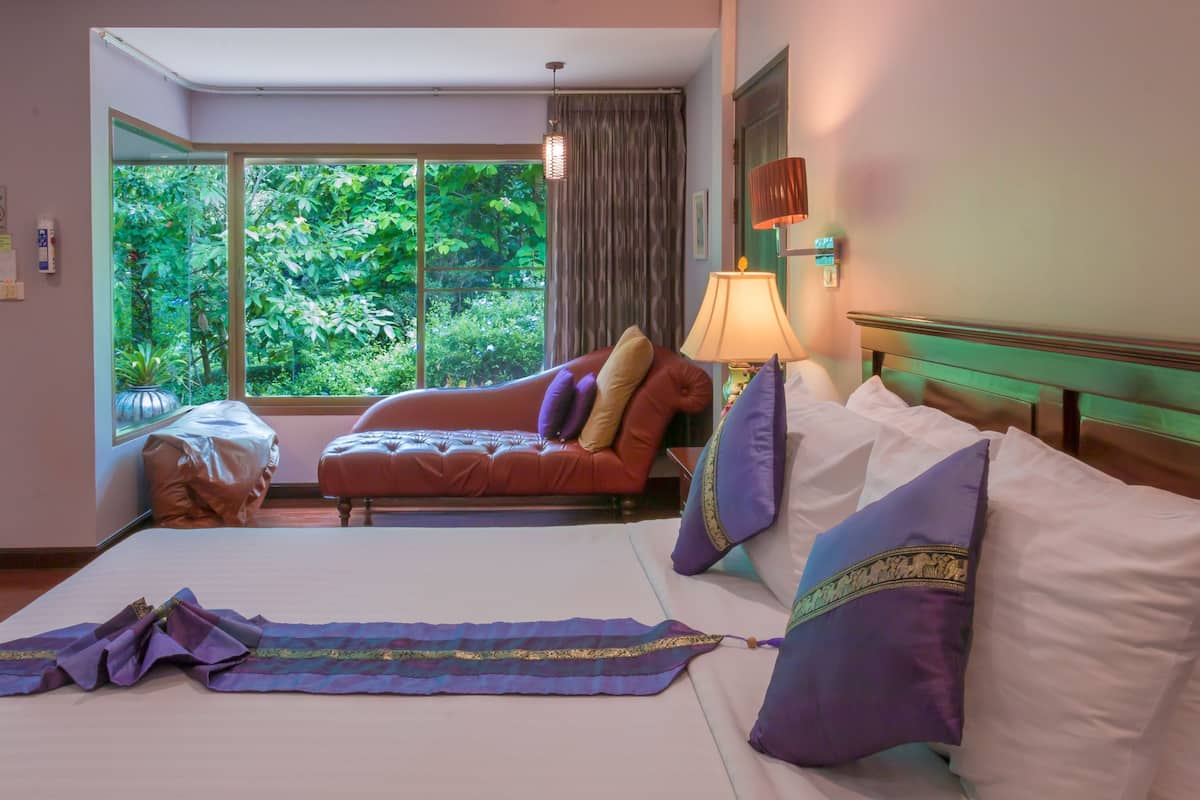 Habitación de hotel con una cama grande, un sofá y vista a un paisaje verde exuberante a través de una ventana.