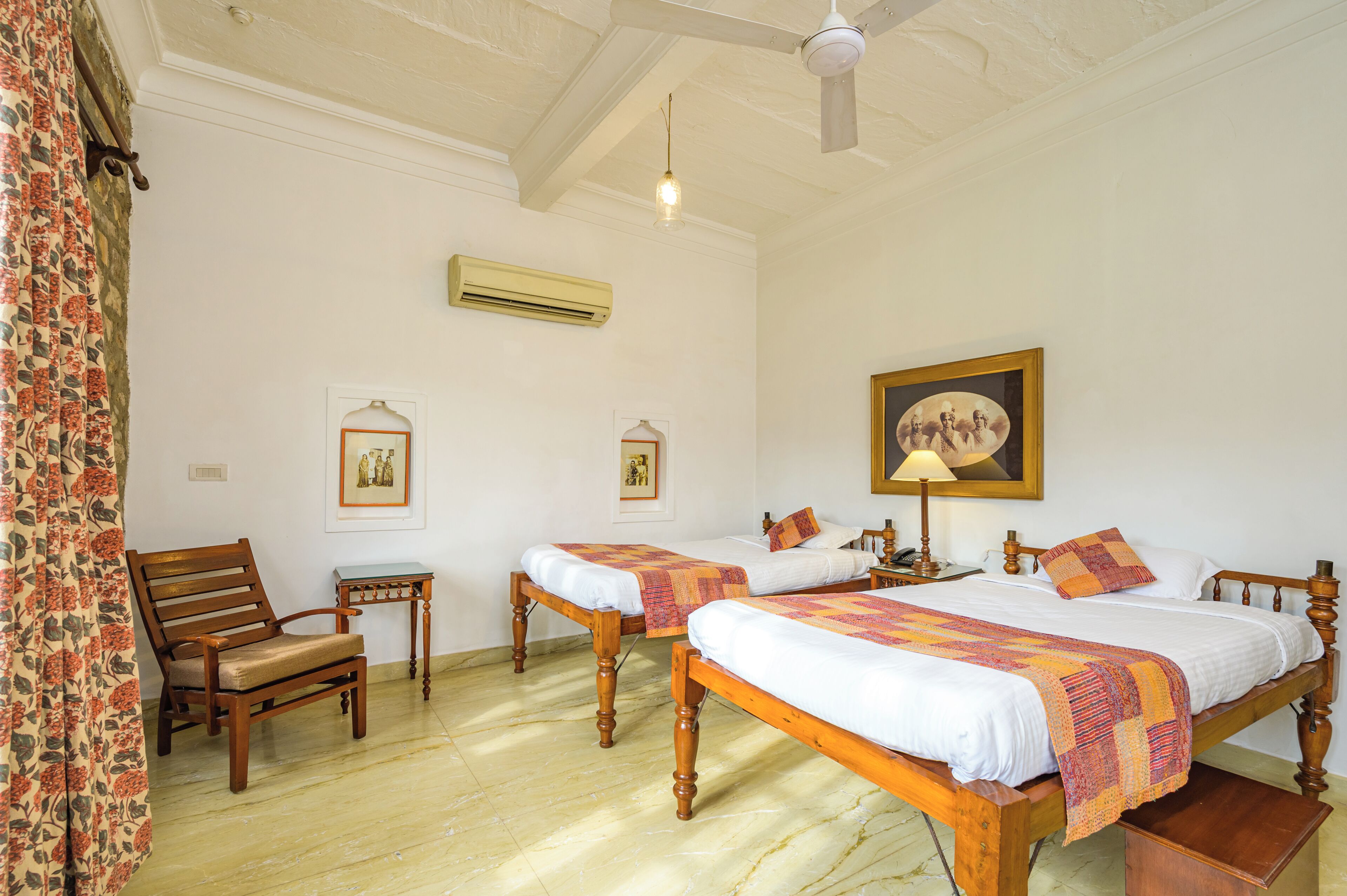 A room with two wooden beds, a chair, a small table, and a ceiling fan.