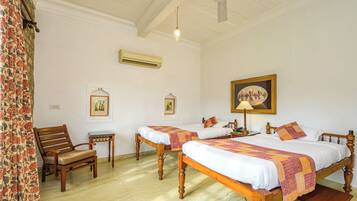 A room with two wooden beds, a chair, a small table, and a ceiling fan.