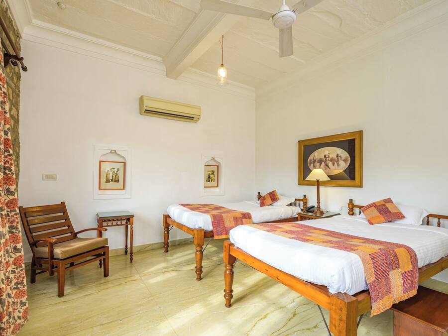 A room with two wooden beds, a chair, a small table, and a ceiling fan.