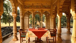 A dining area with a table set for four, surrounded by ornate pillars and a red tablecloth.