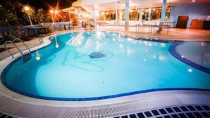A swimming pool with a dolphin design, surrounded by lounge chairs and tables, and a building with large windows in the background.