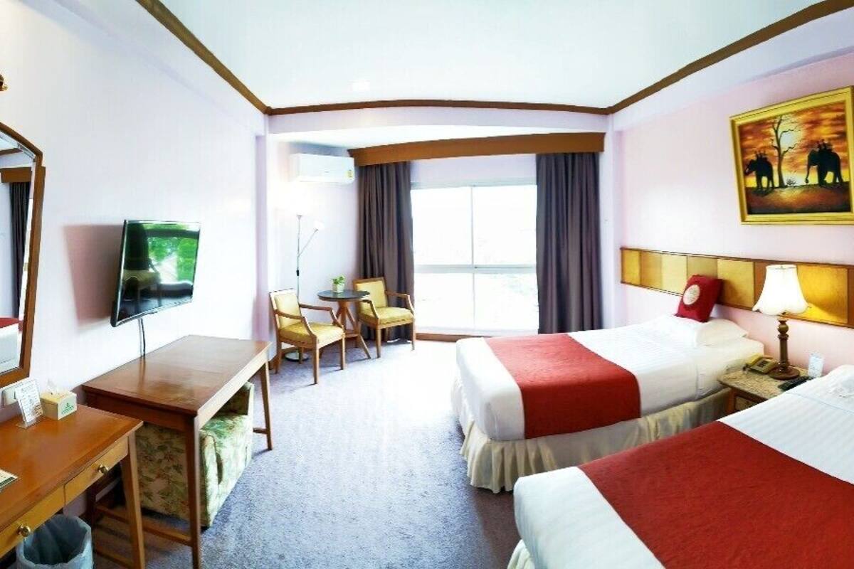 A hotel room with two beds, a desk, a TV, a chair, and a window.
