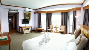A hotel room with a large bed, a desk, a chair, a small table, and a TV.