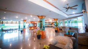 A spacious lobby with a reception desk, seating areas, and large windows offering a view of the outdoors. - The Viangtak Riverside Hotel (Tak)