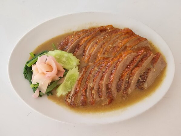 A plate of sliced duck with a crispy skin, accompanied by pickled vegetables and greens. - The Viangtak Riverside Hotel (Tak)