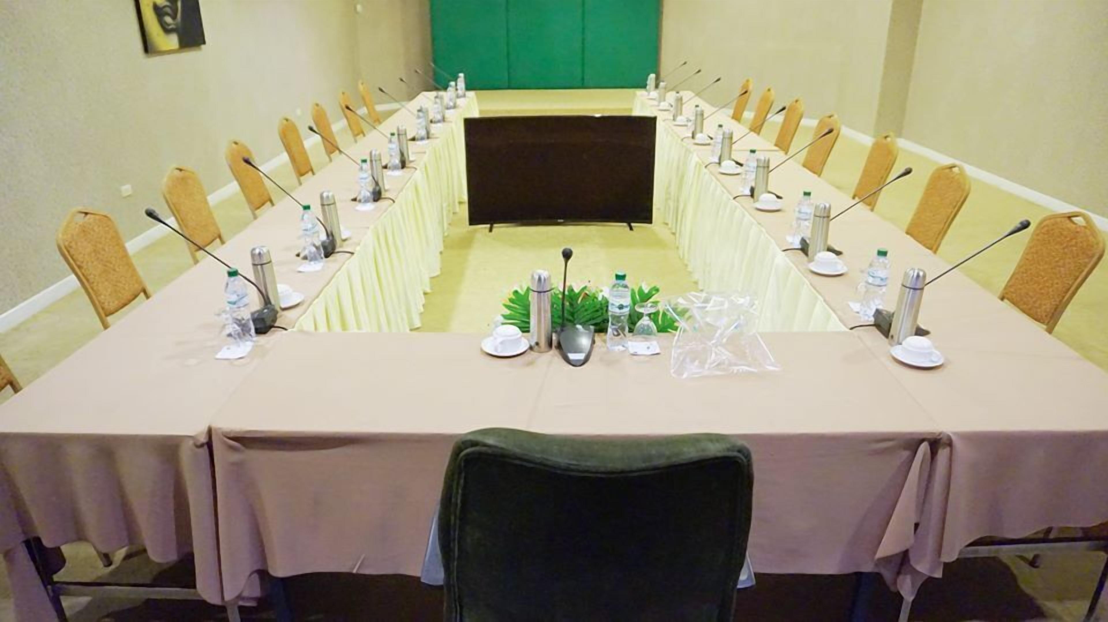 A conference room with a long table, chairs, microphones, water bottles, and a projector screen.