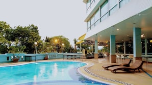 A pool area with lounge chairs, a covered seating area, and a building with large windows. - The Viangtak Riverside Hotel (Tak)