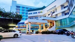 A modern hotel with a multi-story structure, a covered entrance, and a parking area with cars and motorcycles.