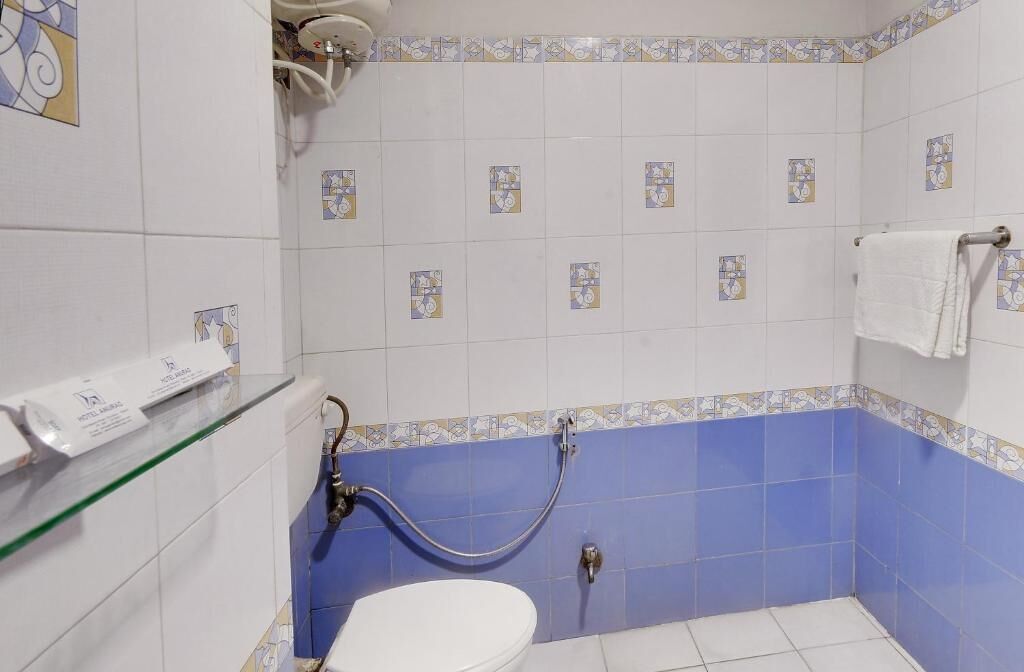 Un baño con inodoro, ducha con manguera y estante de vidrio con toallero.