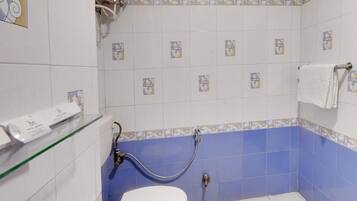 Un baño con inodoro, ducha con manguera y estante de vidrio con toallero.