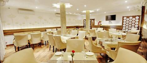A dining area with multiple tables and chairs, a central decorative column, and a television mounted on the wall.