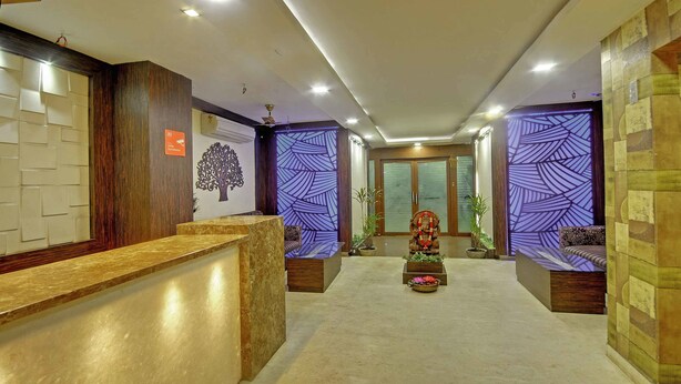 Un espace d’accueil d’hôtel avec un comptoir en marbre, une fresque murale représentant un arbre décoratif et des panneaux muraux à motifs.