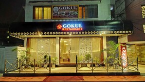 Un restaurant appelé Gokul, doté d’une façade moderne, de panneaux décoratifs en treillis et de plantes en pot à l’entrée.