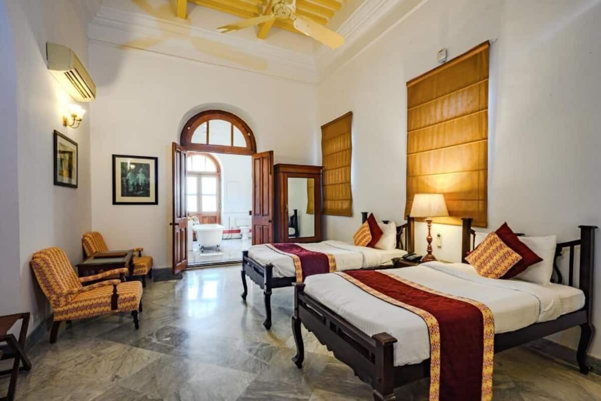 A hotel room with two beds, a sitting area with chairs, a large window, and a door leading to a bathroom.