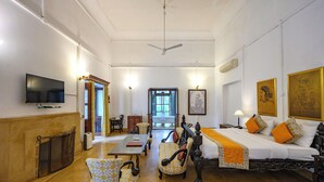 A spacious hotel room with a large bed, two chairs, a table, a television, and a fireplace. - Neemrana's Baradari Palace (Patiala)