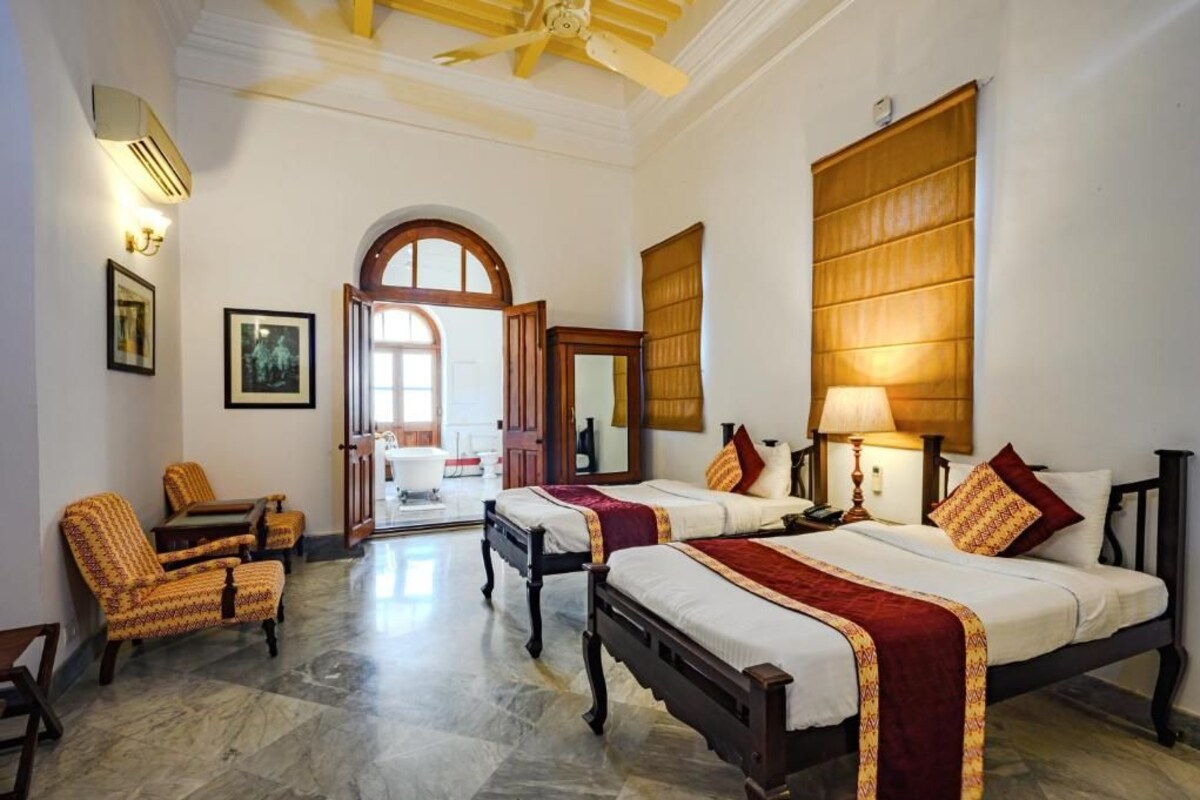 A hotel room with two beds, a sitting area with chairs, a large window, and a door leading to a bathroom.