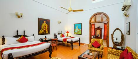 Quarto de hotel com duas camas, um sofá, uma cadeira, uma mesa e um espelho.
