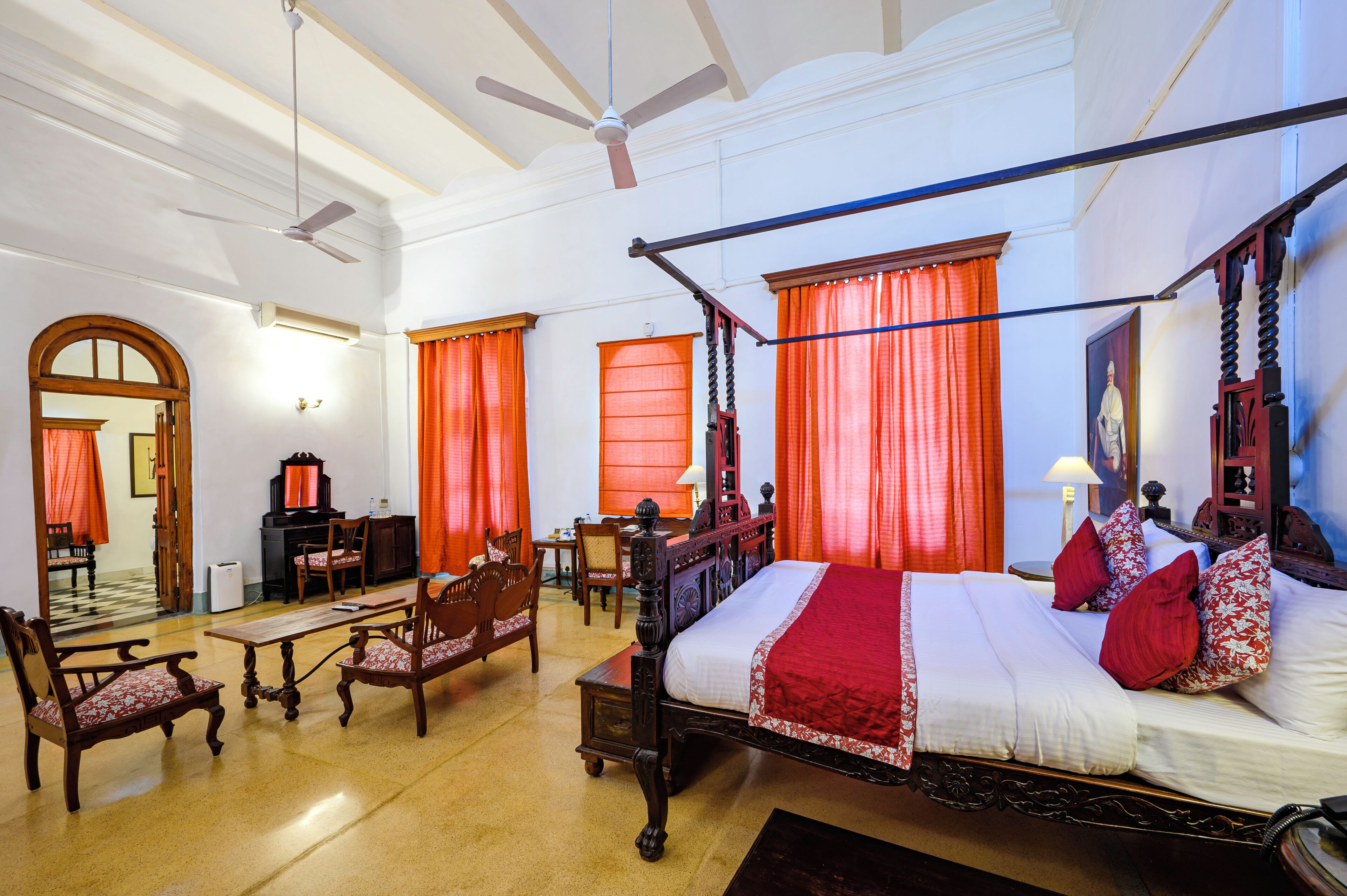 A four-poster bed with red and white bedding, wooden furniture, and orange curtains.