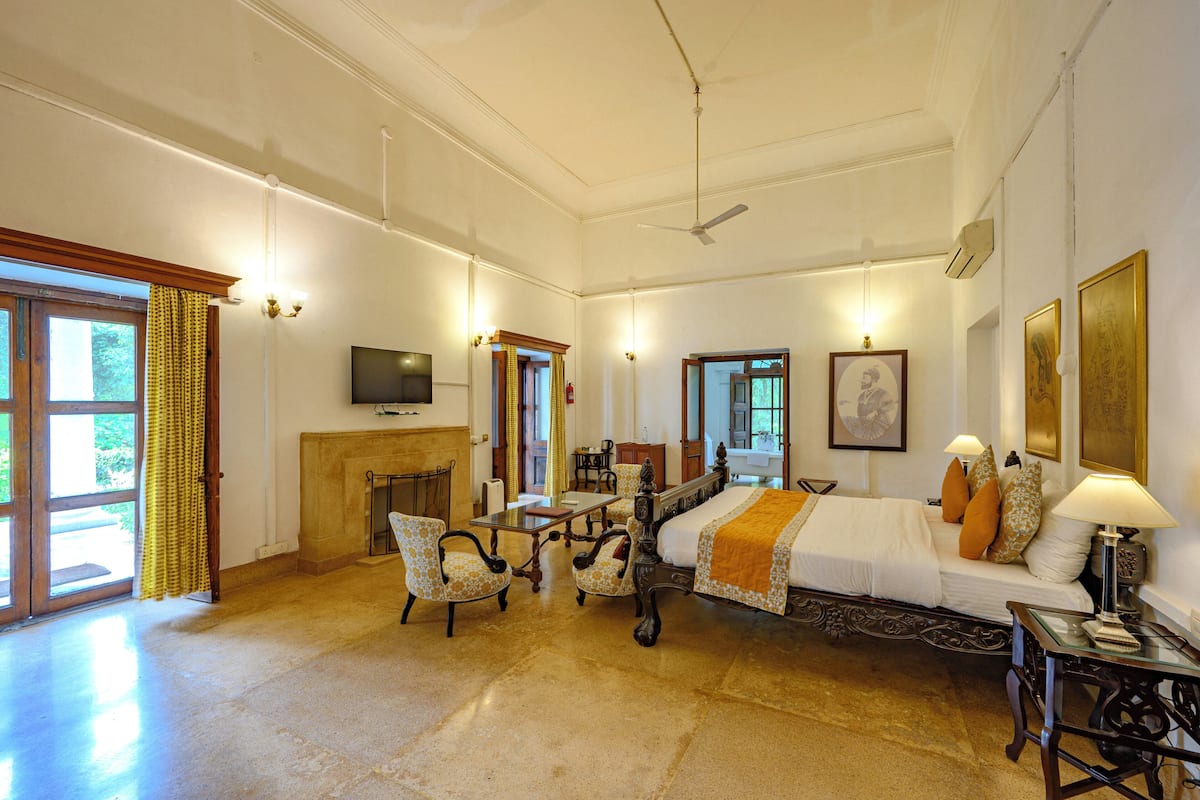 A spacious room with a large bed, two armchairs, a small table, a fireplace, and a television.