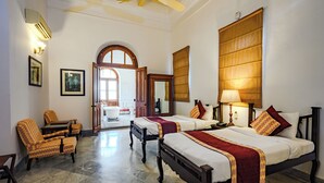 A hotel room with two beds, a sitting area with chairs, a large window, and a bathroom visible through an open door. - Neemrana's Baradari Palace (Patiala)