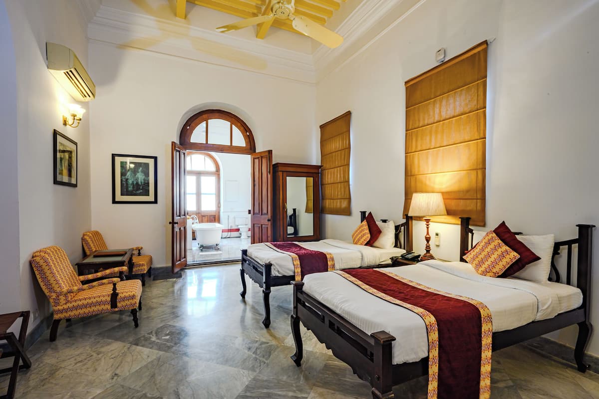 A hotel room with two beds, a sitting area with chairs, a large window, and a bathroom visible through an open door.