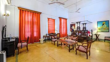 Una habitación amplia con comedor, un ventanal con cortinas rojas, un ventilador de techo y un cuadro en la pared.