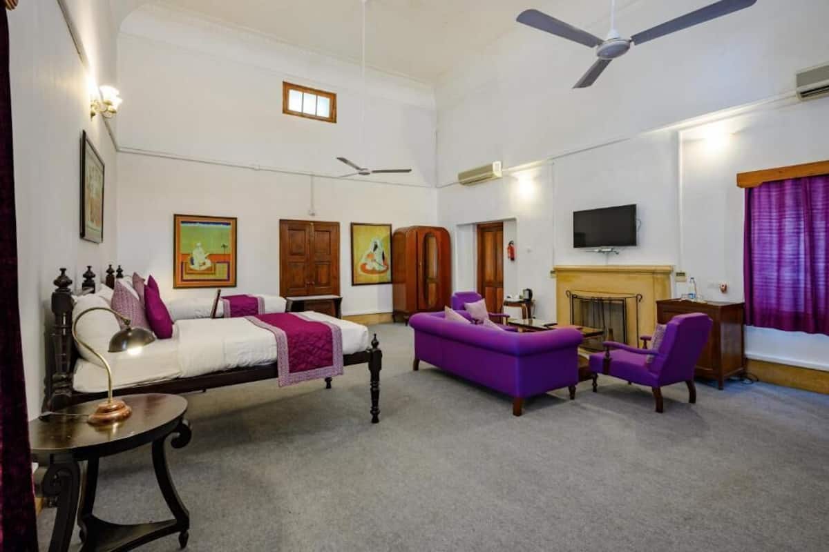 A spacious room with a bed, a purple sofa, a small table, a television, and a fireplace.