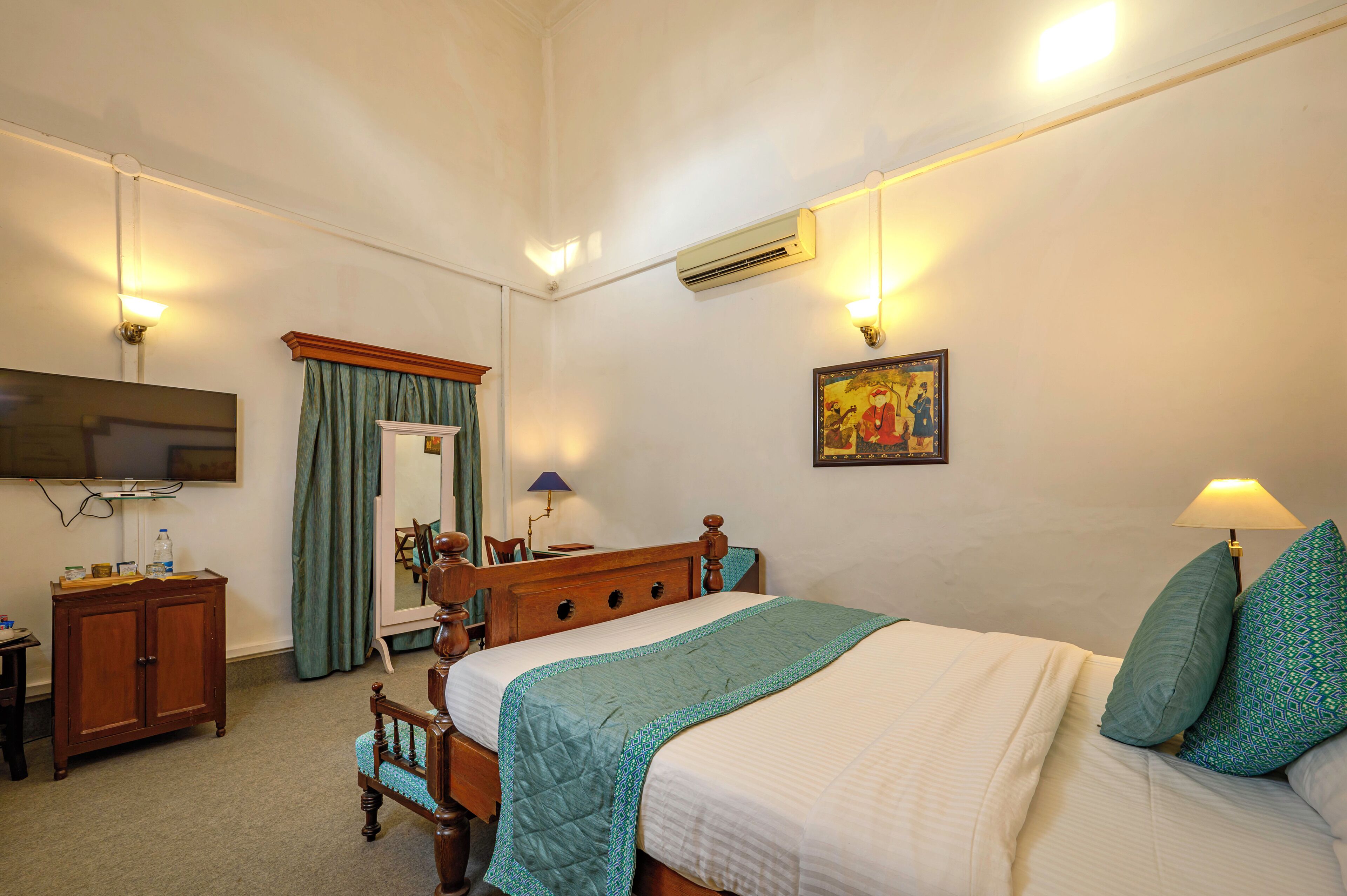 A bedroom with a bed, a wooden dresser, a television, and a mirror.