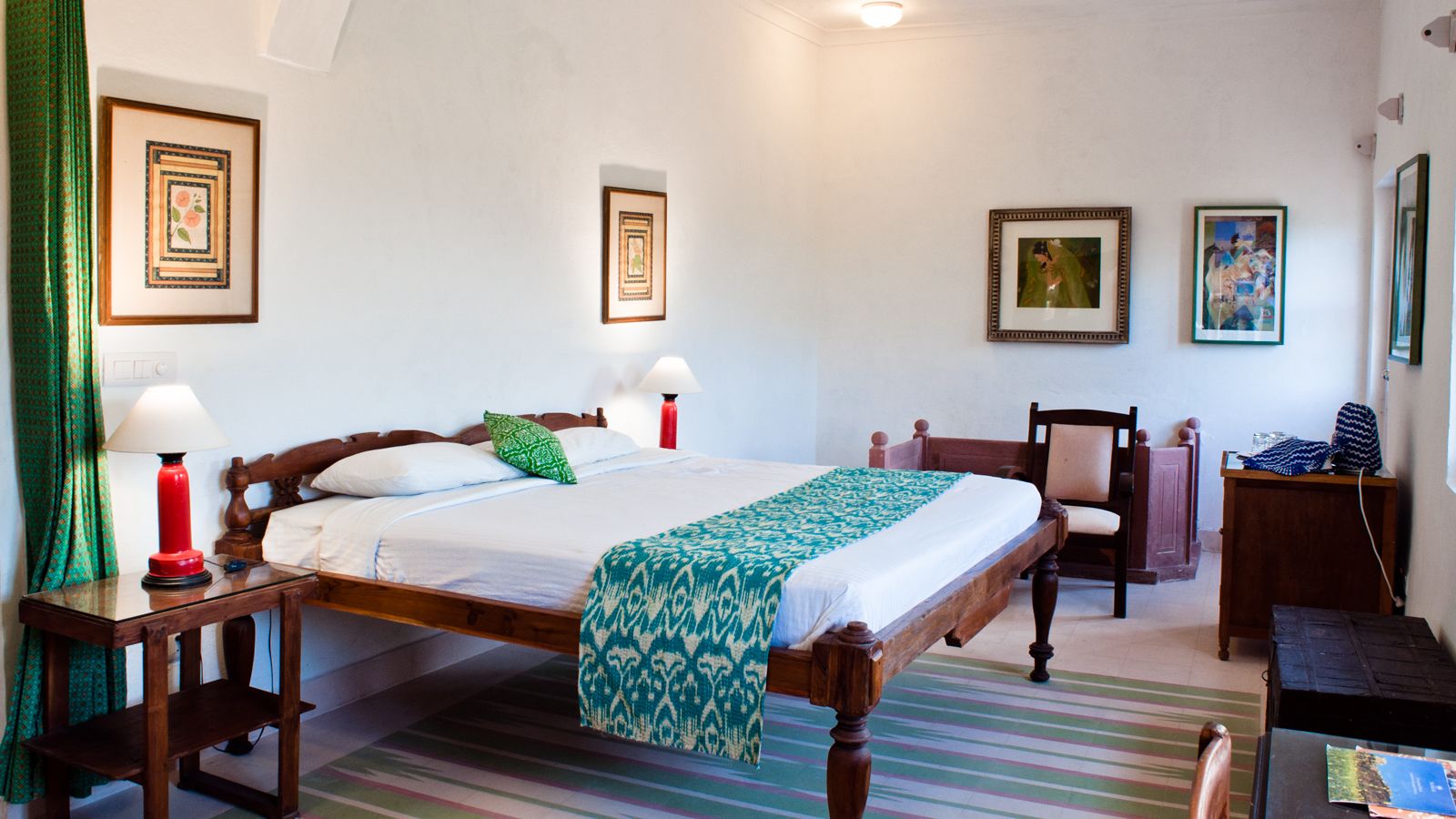 A neatly arranged bedroom with a bed, two bedside tables with lamps, a chair, a small table, and a wall-mounted shelf.