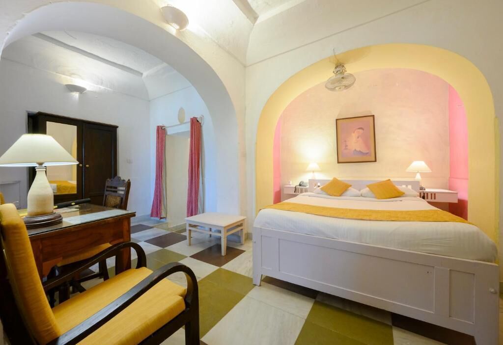 A hotel room with a bed, a desk, a chair, and a small table.