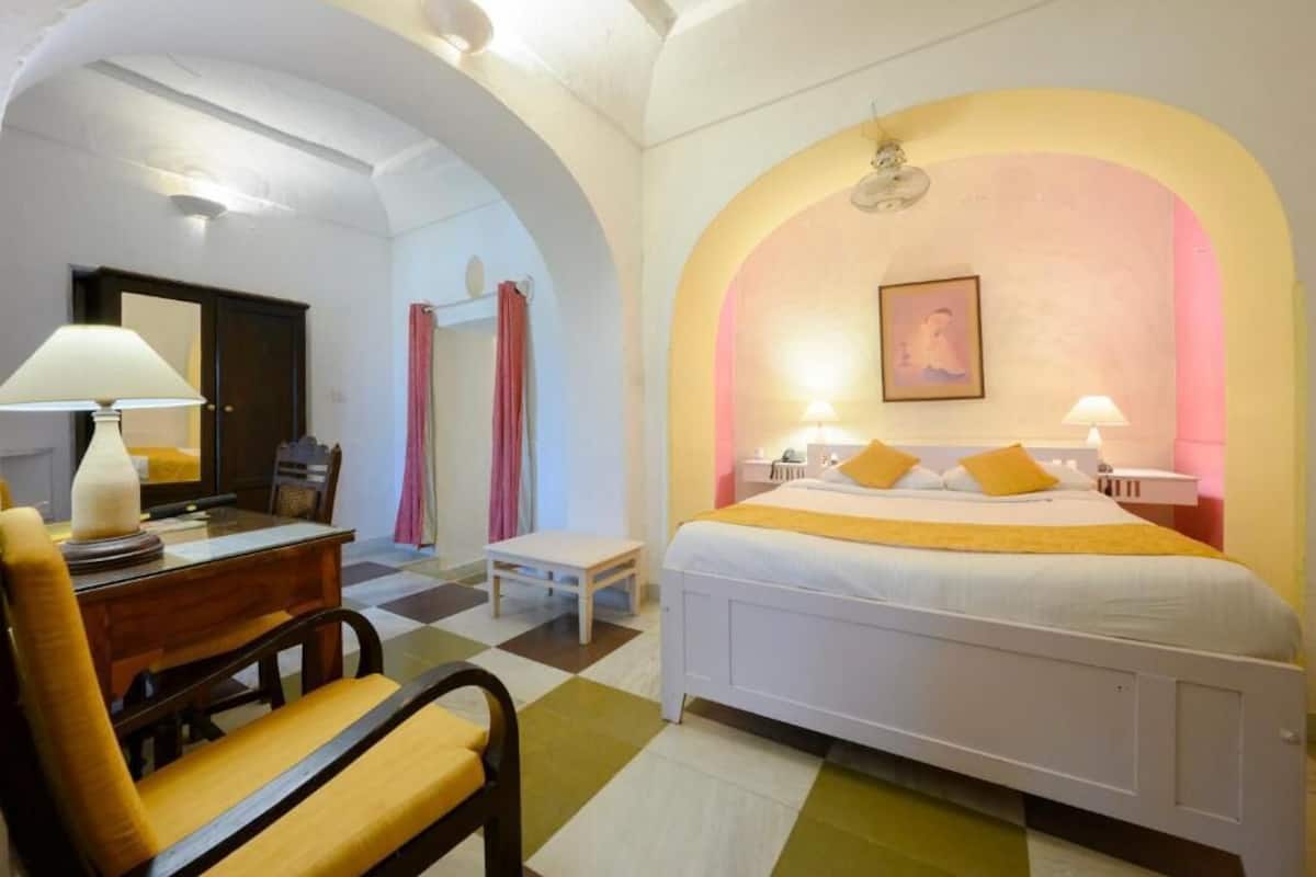 A hotel room with a bed, a desk, a chair, and a small table.