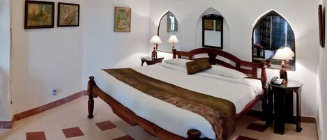 A neatly arranged bedroom with a wooden bed, two bedside tables with lamps, and three wall-mounted paintings.