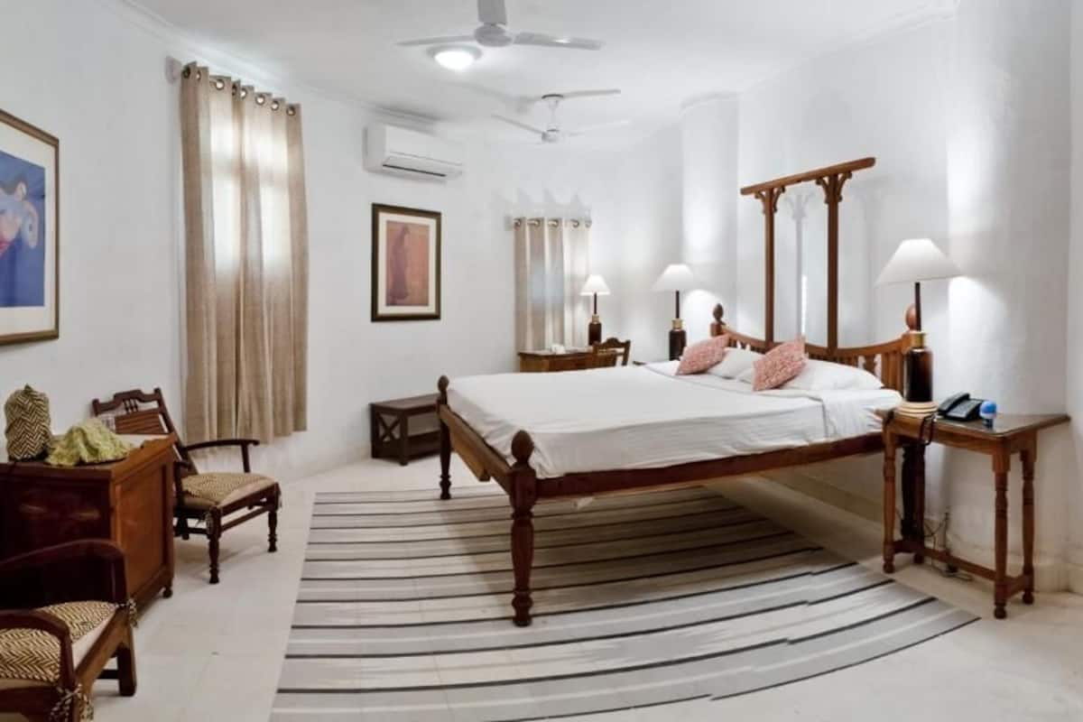A hotel room with a large bed, a desk, two chairs, a mirror, and a ceiling fan.