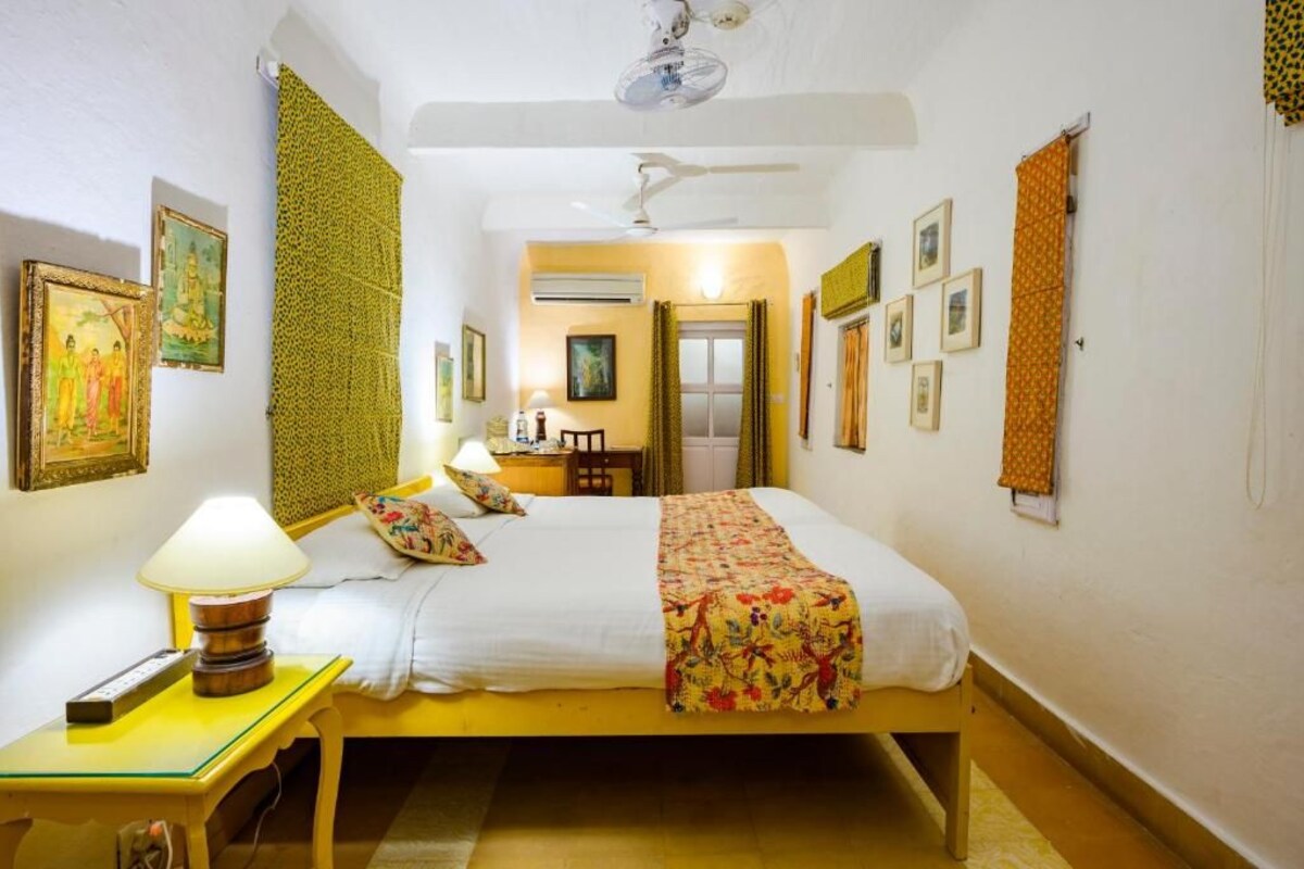 A room with a bed, a bedside table with a lamp, a ceiling fan, and framed pictures on the walls.